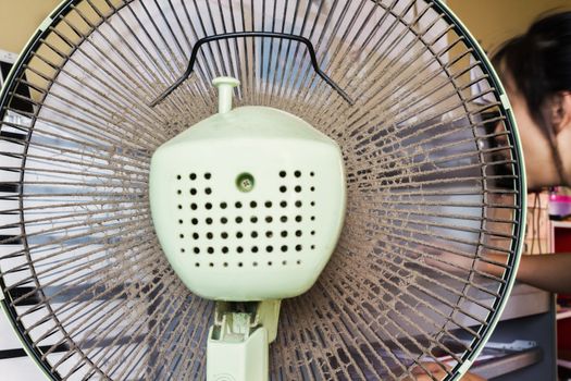 Dusty or unclean portable fan with blurred girl working at table