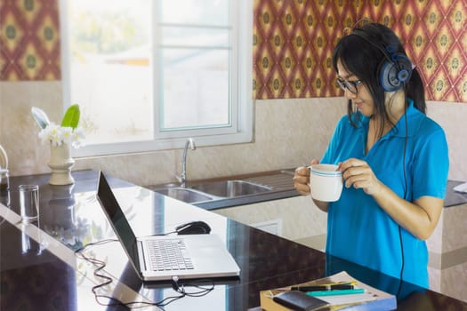 Relaxing life style Asian girl drinking hot drink and watching media on internet with notebook and counter background in home 