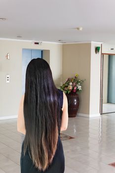 Back side or rare view of black and coloured dry long hair women waiting elevator 