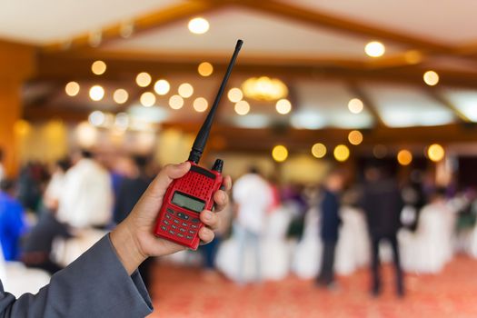 Red radio communication in hand with blurred people in convention hall background and copy space