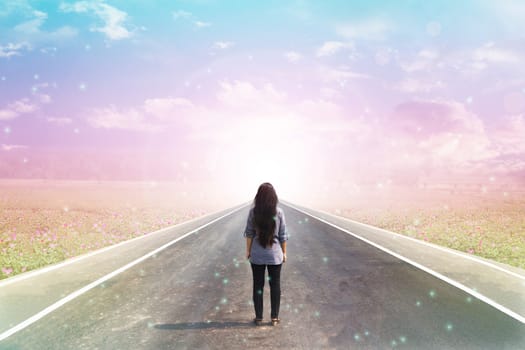  Back or rare of women standing on pavement road with dreamy morning sunlight, flower field  and lensflare background with copy space, concept road to heaven