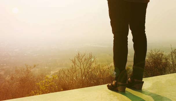 Dramatic colour tone backside of women leg on roof-deck with highland sunrise view blurred background and copy space