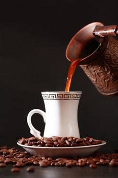 Black coffee flowing from vintage brass coffeepot into cup