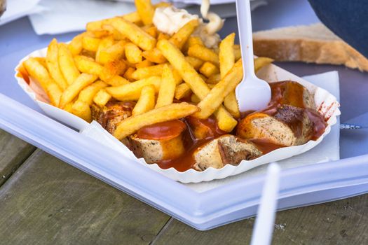 A paper tray with currywurst and French fries  on an old wooden table.