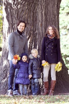 Happy family in autumn park near big tree trunk