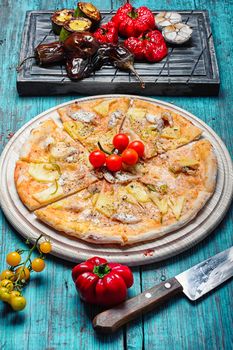 Dining table with pizza and roasted vegetables on stylish cutting board