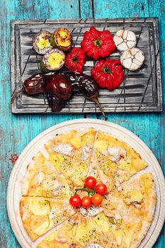 Dining table with pizza and roasted vegetables on stylish cutting board