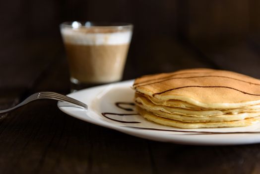 pancakes with chocolate topping and coffee cappuccino with corica on the table