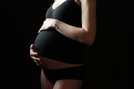 midsection of pregnant woman in black clothes on a black background