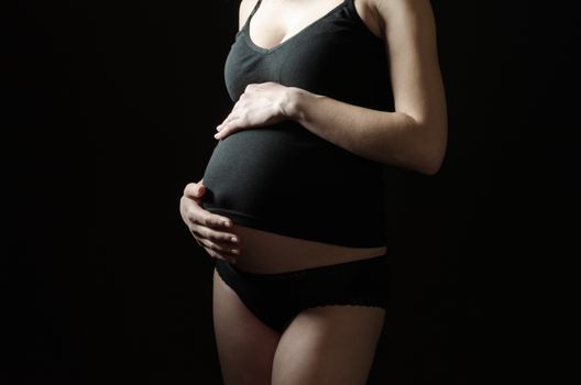 midsection of pregnant woman in black clothes on a black background