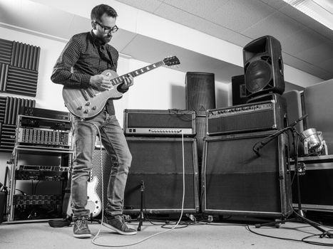 Photo of a man in his late 20's standing in a recording studio playing his electric guitar.