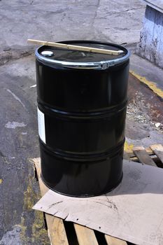 Black metal barrel of combustive-lubricating chemicals is on a wooden pallet at the production site.