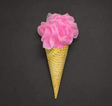Creative concept photo of a waffle cone with a bath puff on black background.