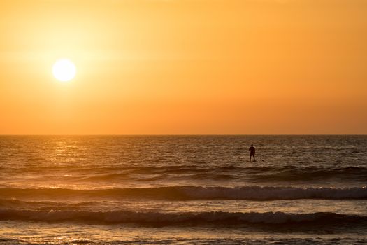 Man paddleboarding in open water at sunset