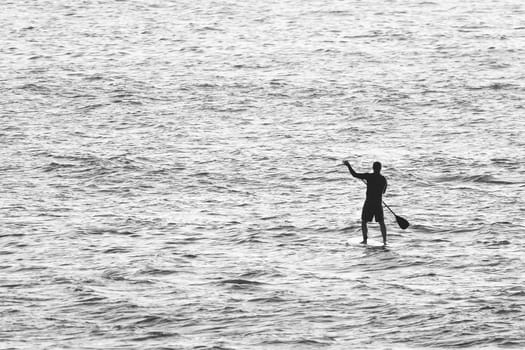 Black and White photo of man on Stand Up Paddle Board surrounded my sea water.