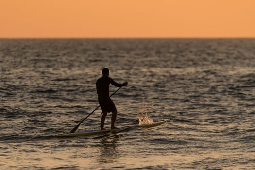 Man paddleboarding in open water at sunset