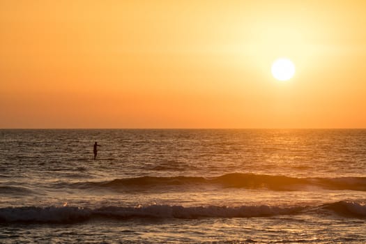 Man paddleboarding in open water at sunset