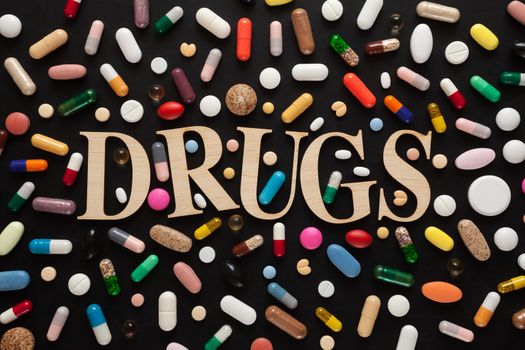 Word DRUGS with wooden letters surrounded by colorful pills