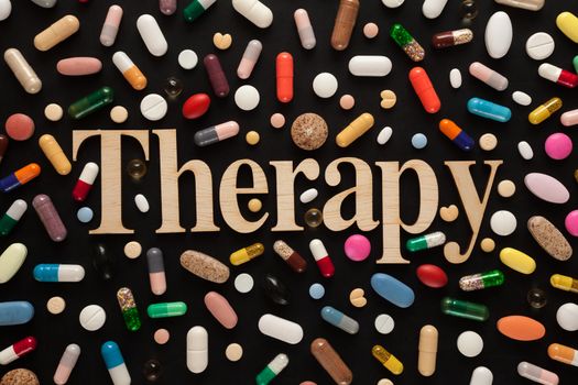 Word THERAPY with wooden letters surrounded by colorful pills