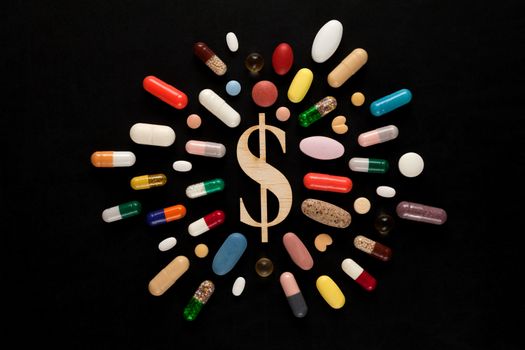 Wooden dollar sign surrounded by colorful pills on black background