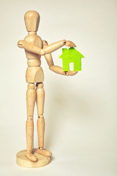Wooden puppet holds small green house on white background