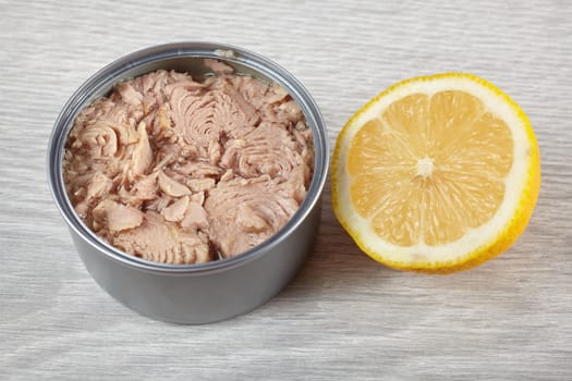 Open tuna tin with half lemon on a gray background