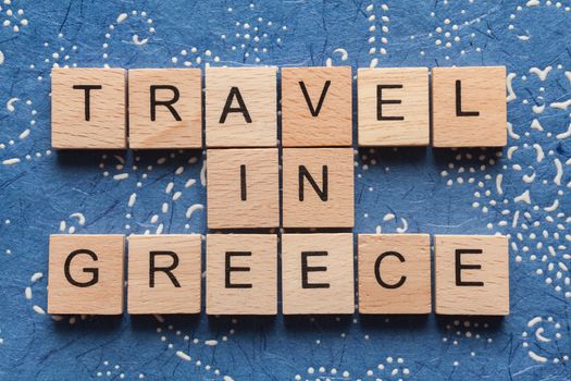 Wooden letters spelling TRAVEL IN GREECE on blue background