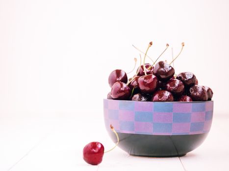 Heap of cherries in dish on white wooden table with copy space.