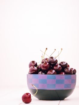 Heap of cherries in dish on white wooden table with copy space. Vertical orientation