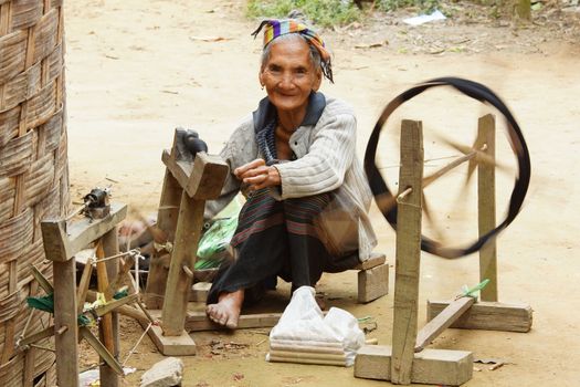 MUANG NGOI, LAOS - FEBRUARY 15, 2016: Old woman spinning on traditional spinning wheel in a minority village on February 15, 2016 in Laos, Asia