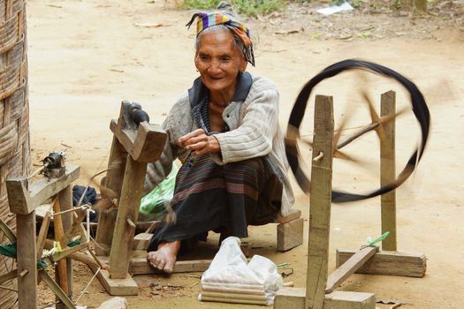 MUANG NGOI, LAOS - FEBRUARY 15, 2016: Old woman spinning on traditional spinning wheel in a minority village on February 15, 2016 in Laos, Asia
