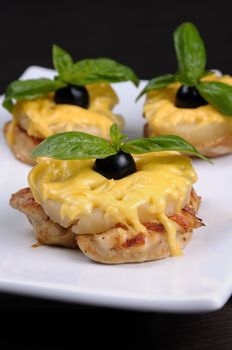 A piece of chicken with pineapple and cheese with olives and basil