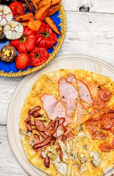 Pizza with meat and bacon and dish of roasted vegetables