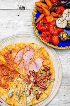 Pizza with meat and bacon and dish of roasted vegetables