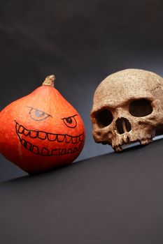 Halloween symbol. Pumpkin head near human skull on dark background