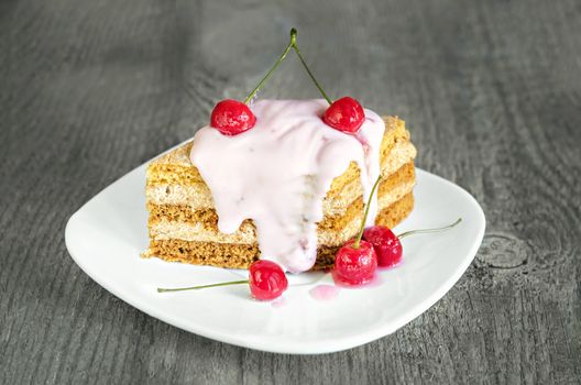 A piece of a layer cake with cherries and yogurt on the plate and wooden background