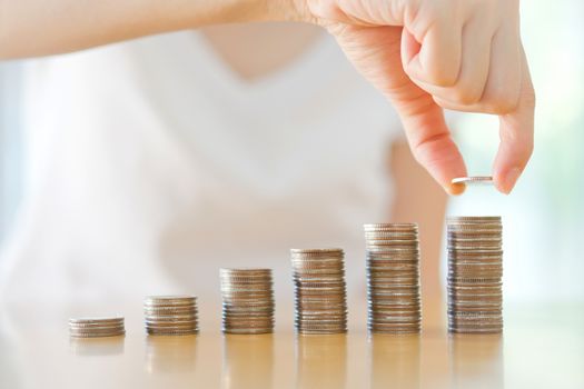 Close-up Of woman Putting Coin To Rising Stack Of Coins