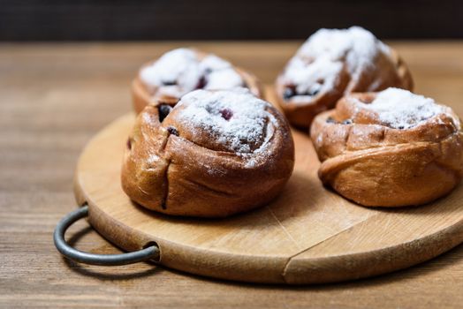 bun with currants covered with powdered sugar lay on a chopping board brown