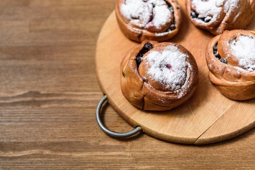 bun with currants covered with powdered sugar lay on a chopping board brown