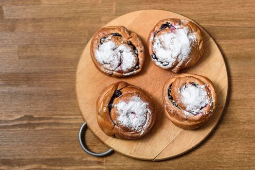 bun with currants covered with powdered sugar lay on a chopping board brown