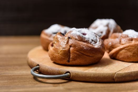 bun with currants covered with powdered sugar lay on a chopping board brown