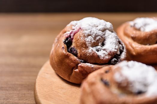 bun with currants covered with powdered sugar lay on a chopping board brown
