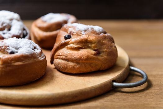 bun with currants covered with powdered sugar lay on a chopping board brown