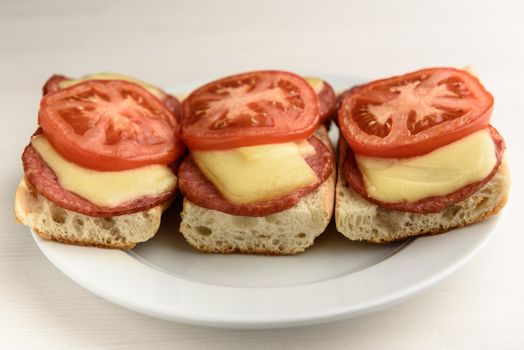 hot sandwiches with melted cheese sausage, salami and tomatoes