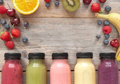 Assorted flavoured smoothie juices in bottles over a wooden background with fruit