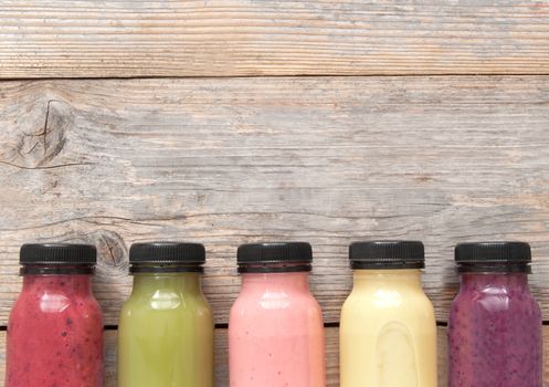 Assorted flavoured smoothie juices in bottles over a wooden background