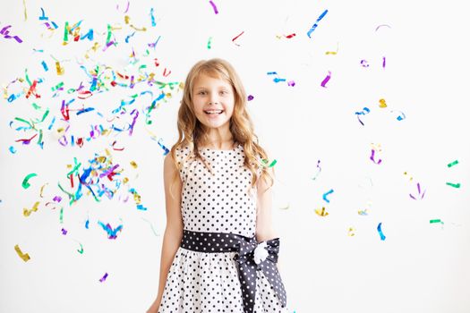 Little girl jumping and having fun celebrating birthday. Portrait of a child throws up multi-colored tinsel and confetti. Positive emotions. Happy excited laughing kid under sparkling confetti shower