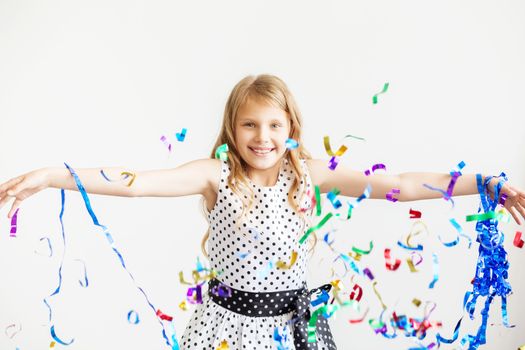 Little girl jumping and having fun celebrating birthday. Portrait of a child throws up multi-colored tinsel and confetti. Positive emotions. Happy excited laughing kid under sparkling confetti shower