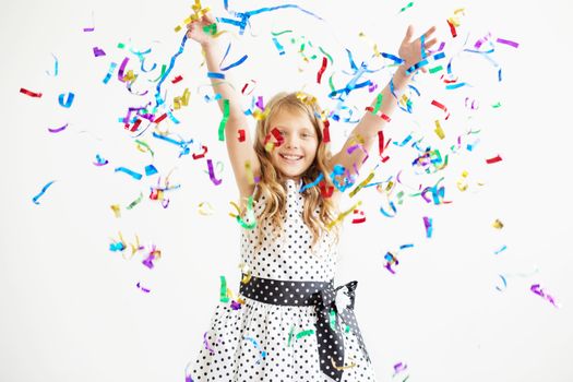 Little girl jumping and having fun celebrating birthday. Portrait of a child throws up multi-colored tinsel and confetti. Positive emotions. Happy excited laughing kid under sparkling confetti shower