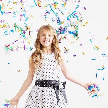 Little girl jumping and having fun celebrating birthday. Portrait of a child throws up multi-colored tinsel and confetti. Positive emotions. Happy excited laughing kid under sparkling confetti shower